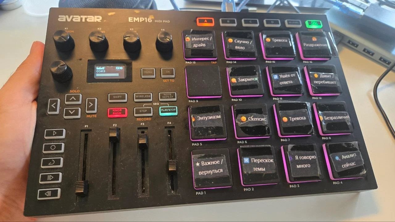 My Avatar EMP16 in my hand. The pads carry stickers with the tags in Russian: interest or drive, bored or flat, anxious, irritated, closed up, dodged, pushing or interrupting, enthusiasm, skepticism, worry, indifference, important or return, topic jump, I talk too much, analyze now. Four knobs and four faders on the left.