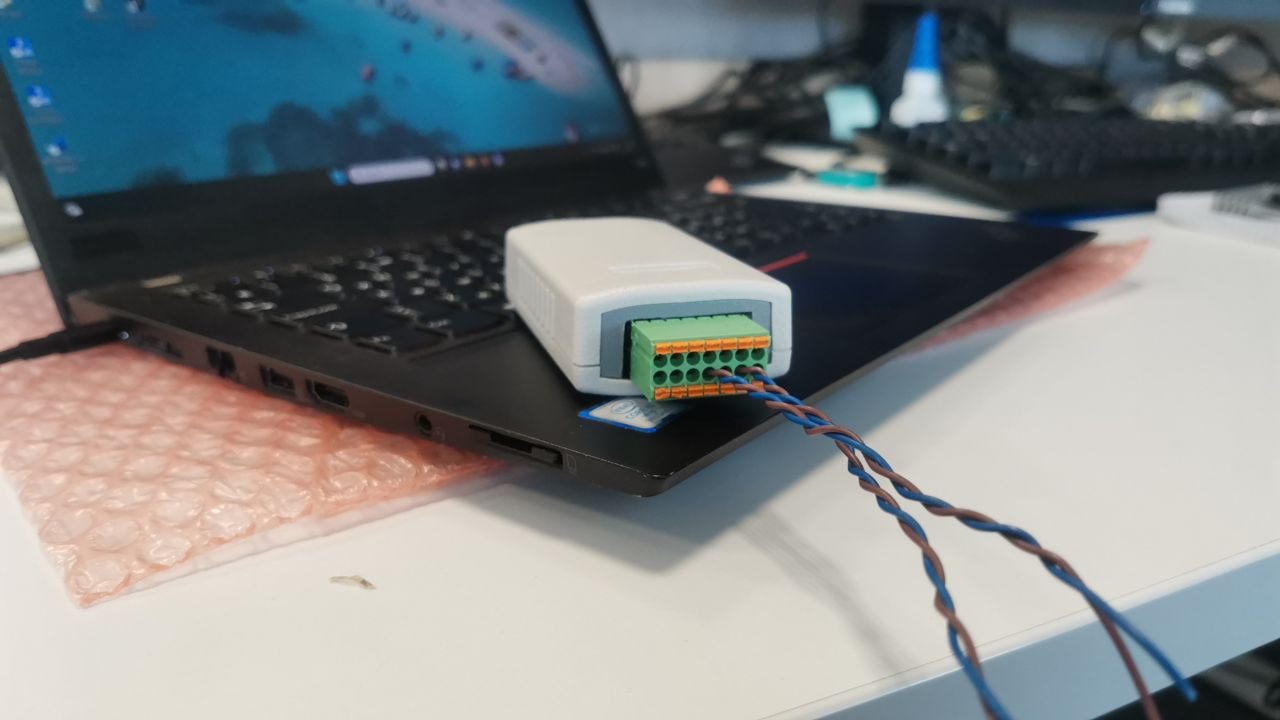 The V6 controller in a light plastic enclosure with a green spring terminal block and wires connected, on a laptop