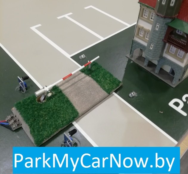 A model car park with a barrier, marked spaces and a building, labelled ParkMyCarNow.by